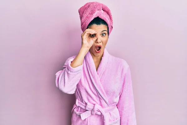 若いヒスパニック系の女性がシャワータオルキャップとバスローブを着用し 驚きの顔でショックを受けたOkジェスチャーを行うと 目の指を見て 信じられない表現 — ストック写真