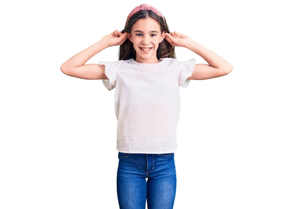 可爱的惊慌失措的小女孩穿着随意的白色T恤 微笑着用手指拉耳朵 滑稽的手势 试镜问题 — 图库照片