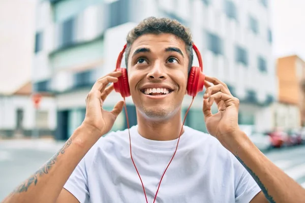 年轻的拉丁男子笑着高兴地使用耳机走在城市 — 图库照片
