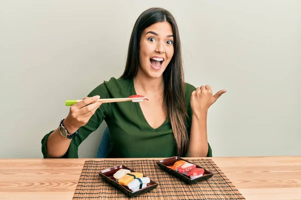 Joven Morena Comiendo Sushi Sentada Mesa Apuntando Con Pulgar Hacia — Foto de Stock