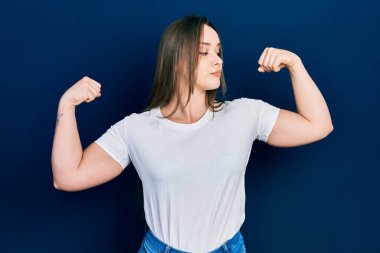 Sıradan beyaz tişört giyen genç İspanyol kız gururla gülümseyen kol kaslarını gösteriyor. fitness konsepti. 