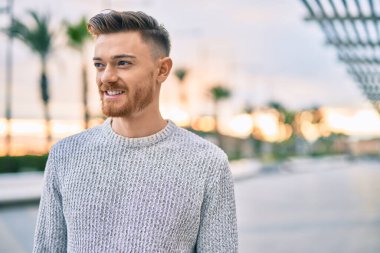 Genç beyaz adam gülümseyerek şehirde mutlu mesut duruyor..