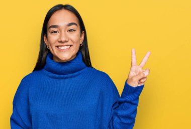 Sıradan bir kazak giyen genç Asyalı kadın kameraya bakıp gülümseyen ve zafer işareti yapan. İki numara.. 