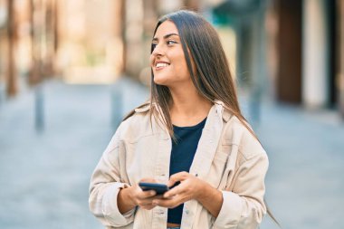 Genç İspanyol kız şehirde akıllı telefon kullanarak mutlu bir şekilde gülümsüyor..