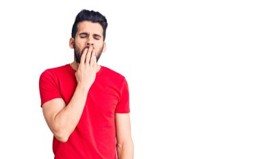 Sıradan tişörtler giyen sakallı genç yakışıklı adam ağzıyla esnemekten sıkılmış. Huzursuz ve uykulu.. 