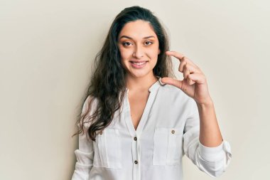 Güzel bir ortadoğulu kadın, günlük kıyafetler giymiş, gülümseyen ve el hareketleriyle el hareketi yapan, parmaklarıyla işaret eden ve kameraya bakan. ölçüm kavramı. 