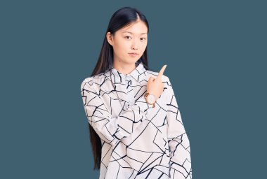 Genç, güzel, Çinli bir kadın, gündelik tişörtler giyip, el parmaklarıyla kenarı işaret ederek ciddi ve sakin bir yüz ifadesi sergiliyor. 