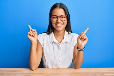 Güzel İspanyol kadın, gündelik giysiler giyip masaya oturmuş, kendine güvenerek farklı yönleri işaret ediyor. reklam için kopyalama alanı 