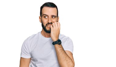 Sakallı, günlük beyaz t-shirt giyen, gergin ve elleri ağızdan tırnak yiyen genç bir adam. anksiyete. 