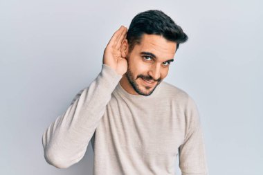 Gündelik kıyafetler giyen, ağzı kulaklarında gülümseyen, dedikoduları ve dedikoduları dinleyen genç İspanyol bir adam. Sağırlık kavramı. 