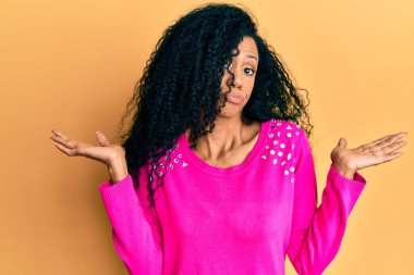 Orta yaşlı Afro-Amerikalı kadın, gündelik giysiler giyiyor, habersiz ve kolları açık, hiçbir fikrim yok ve şüpheli bir yüz var.. 