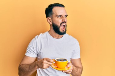 Sakallı genç adam kızgın ve kızgın bir şekilde kahveyi yudumluyor ve öfkeyle bağırıyor. öfke ve agresif konsept. 