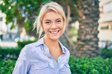 Parkta yürürken gülümseyen genç sarışın kadın..