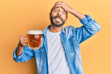 Uzun saçlı ve sakallı çekici bir adam yarım litre bira içiyor. Stresli ve hayal kırıklığına uğramış, şaşırmış ve kızgın bir yüzü var. 