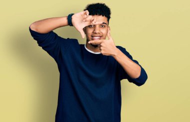 Gündelik kıyafetler giyen, gülümseyen ve mutlu yüzlü elleri ve parmakları olan genç Afro-Amerikan bir adam. yaratıcılık ve fotoğrafçılık kavramı. 