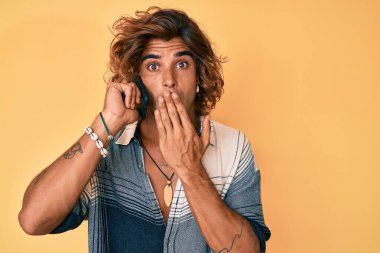 Genç İspanyol bir adam akıllı telefonda konuşuyor. Ağzını eliyle kapatıyor. Şok geçiriyor ve hata yapmaktan korkuyor. şaşırmış ifade 