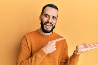 Kış süveteri giyen sakallı genç adam kameraya hayret ediyor ve gülümsüyor.. 