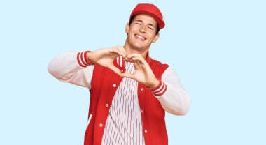 Handsome caucasian man wearing baseball uniform smiling in love doing heart symbol shape with hands. romantic concept. 