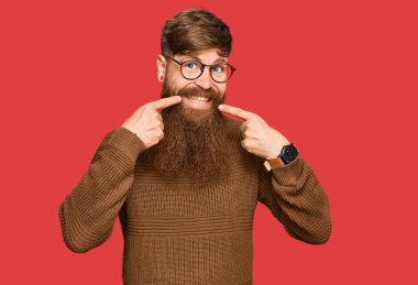 Genç İrlandalı kızıl elbiseli ve gözlüklü neşeli gülümseyen ve parmaklarıyla ve ağzıyla işaret eden adam. diş sağlığı kavramı. 