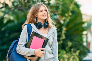 Parkta kulaklık takarak mutlu gülümseyen güzel beyaz öğrenci..