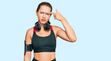 Güzel sarışın kadın spor kıyafetleri giyiyor ve kulaklık takıyor. Alnındaki sivilceden mutsuz olduğunu gösteriyor. Siyah nokta enfeksiyonu. sivilce ve deri problemi 