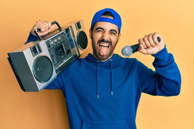 Genç İspanyol adam elinde teyp ile mikrofonla şarkı söylüyor. Dilini çıkarıp komik bir ifade takınıyor.. 