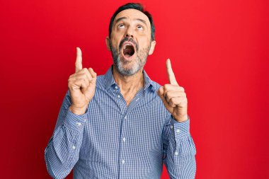 Orta yaşlı, sıradan kıyafetler giyen, şaşkın şaşkın bakan, parmaklarıyla işaret eden ve kollarını kaldıran bir İspanyol.. 