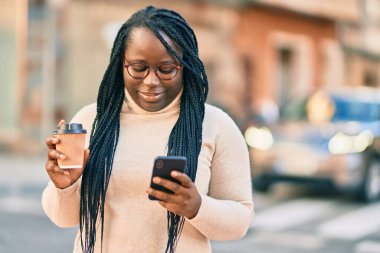 Genç Afrikalı Amerikalı kadın akıllı telefon kullanıyor ve şehirde kahve içiyor..