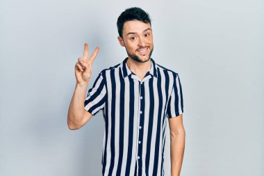 Gündelik kıyafetler giyen genç İspanyol adam iki numarayı gösterip işaret ederken kendinden emin ve mutlu bir şekilde gülümsüyor.. 