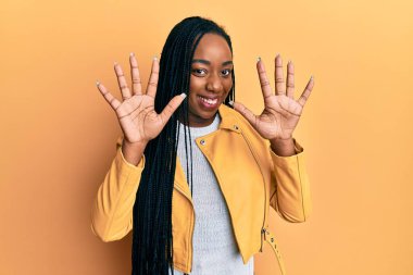 Genç Afro-Amerikalı kadın rahat bir ceket giyer ve parmaklarını 10 numaraya doğrultur, gülümser ve mutlu olur.. 