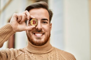 Genç beyaz adam mutlu bir şekilde gülümsüyor. Bitcoin 'i şehrin gözü önünde tutuyor..