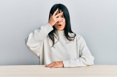 Kâküllü, sıradan giysiler giymiş genç esmer kadın masanın üzerinde oturuyor. Şok olmuş bir şekilde yüzünü ve gözlerini eliyle kapatıyor, parmaklarından bakıyor. 