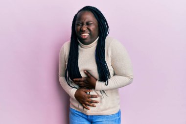 Saçları örgülü genç siyahi bir kadın, elleri karnında, sıradan bir kazak giyiyor çünkü mide bulantısı, acı verici bir hastalık kendini iyi hissetmiyor. Ağrı kavramı. 