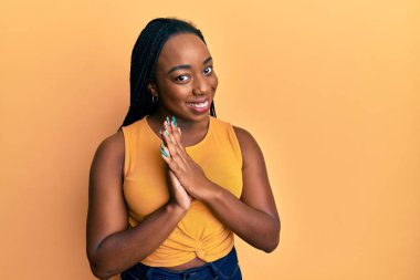 Afro-Amerikalı genç bir kadın günlük kıyafetler giyip ellerinin birliğiyle dua ediyor af diliyor kendinden emin bir şekilde gülümsüyor.. 