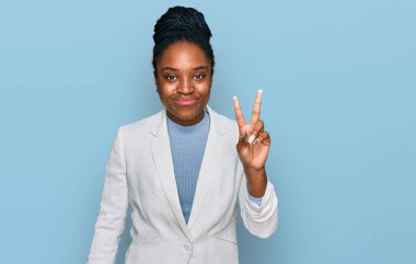 İş kıyafetleri giymiş, gülümseyen, parmaklarını zafer işareti yaparken gösteren genç Afrikalı Amerikalı kadın. İki numara.. 