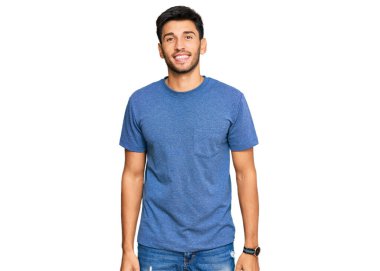 Gündelik kıyafetler giyen yakışıklı genç adam pozitif ve mutlu görünüyor. Duruyor ve gülümsüyor. Kendine güvenen bir gülümsemeyle dişlerini gösteriyor. 