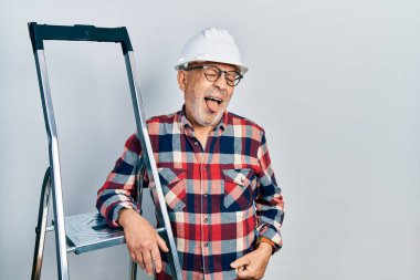 İnşaat merdivenlerine yakın, şapkalı, dilinde komik bir ifade olan yakışıklı bir tamirci. duygu kavramı. 