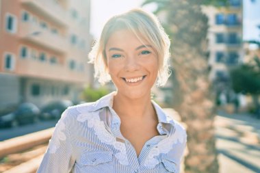 Parkta yürürken gülümseyen genç sarışın kadın..