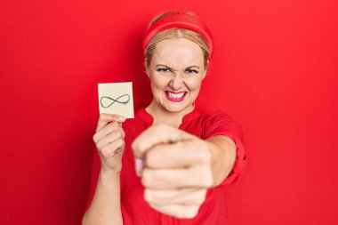 Elinde sonsuz sembol tutan genç sarışın kadın sinirlenmiş ve sinirlenmiş öfkeyle bağırıyor, öfkeyle ve el kaldırarak çılgınca bağırıyor. 