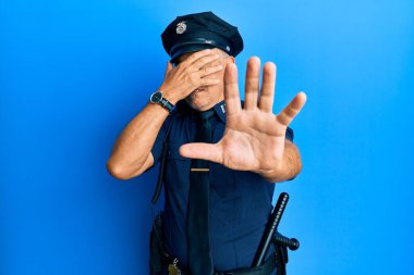 Yakışıklı, olgun, polis üniforması giyen, elleriyle gözlerini kapatan, üzgün ve korku ifadeleriyle jestler yapan bir adam. utangaç ve olumsuz kavram. 