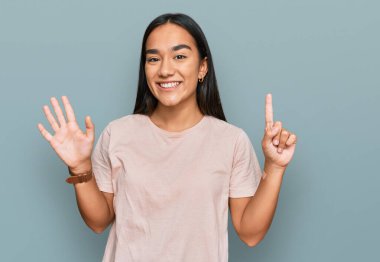 Genç Asyalı kadın gündelik giysiler giyip altı numaralı parmaklarıyla işaret ederken kendinden emin ve mutlu bir şekilde gülümsüyor.. 
