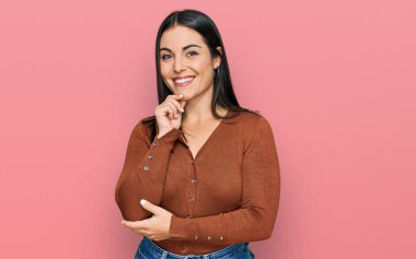 Günlük kıyafetler giyen genç İspanyol kadın kameraya kendinden emin bakıyor kollarını kavuşturup gülümseyerek ve çenesini kaldırarak. Olumlu düşünmek. 