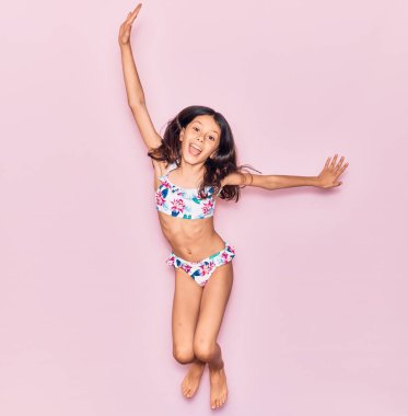 Sevimli İspanyol çocuk tatilde bikini giymiş mutlu bir şekilde gülümsüyor. İzole edilmiş pembe arka planda yüzünde gülümsemeyle zıplıyorsun.