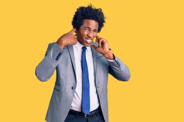 Afro saçlı, iş ceketi giyen, kulaklarını parmaklarıyla kulaklarını kapatan, gürültülü müzik sesi için rahatsız edici ifadeleri olan yakışıklı Afro-Amerikalı bir adam. sağır kavramı. 