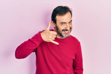 Orta yaşlı İspanyol bir adam günlük kıyafetler giyip gülümsüyor telefonla el ve parmak hareketleri yapıyor telefonda konuşuyor gibi. iletişim kavramları. 