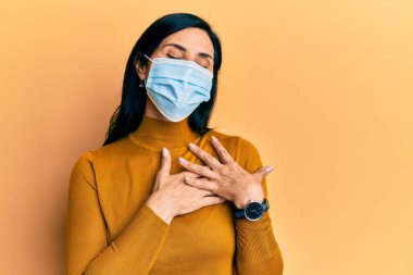 Tıbbi maske takan, elleri göğsünde gülümseyen, gözleri kapalı, yüzünde minnet ifadesi olan beyaz bir kadın. sağlık kavramı. 