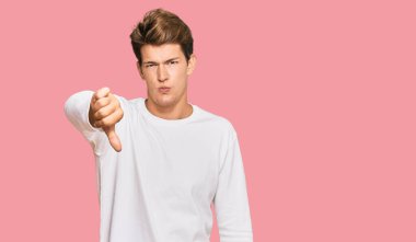 Handsome caucasian man wearing casual white sweater looking unhappy and angry showing rejection and negative with thumbs down gesture. bad expression. 