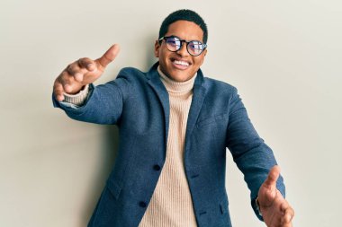 Zarif kıyafetler ve gözlük takmış genç yakışıklı İspanyol adam kameraya bakıp sarılmak için kollarını açmış gülümsüyor. Mutluluğu kucaklayan neşeli bir ifade.. 