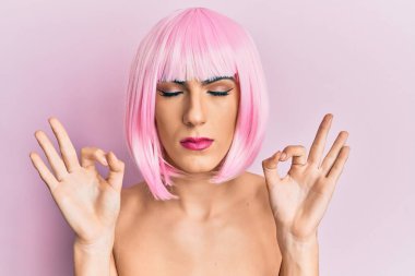 Pembe peruk takan, gülümseyen, gözleri kapalı meditasyon yapan genç bir adam parmaklarıyla meditasyon yapıyor. yoga konsepti. 