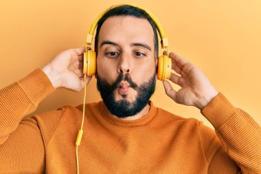 Sakallı genç adam kulaklık takarak müzik dinliyor. Ağızlarıyla balık yüzü yapıyor ve şaşı bakıyor. Deli ve komik.. 